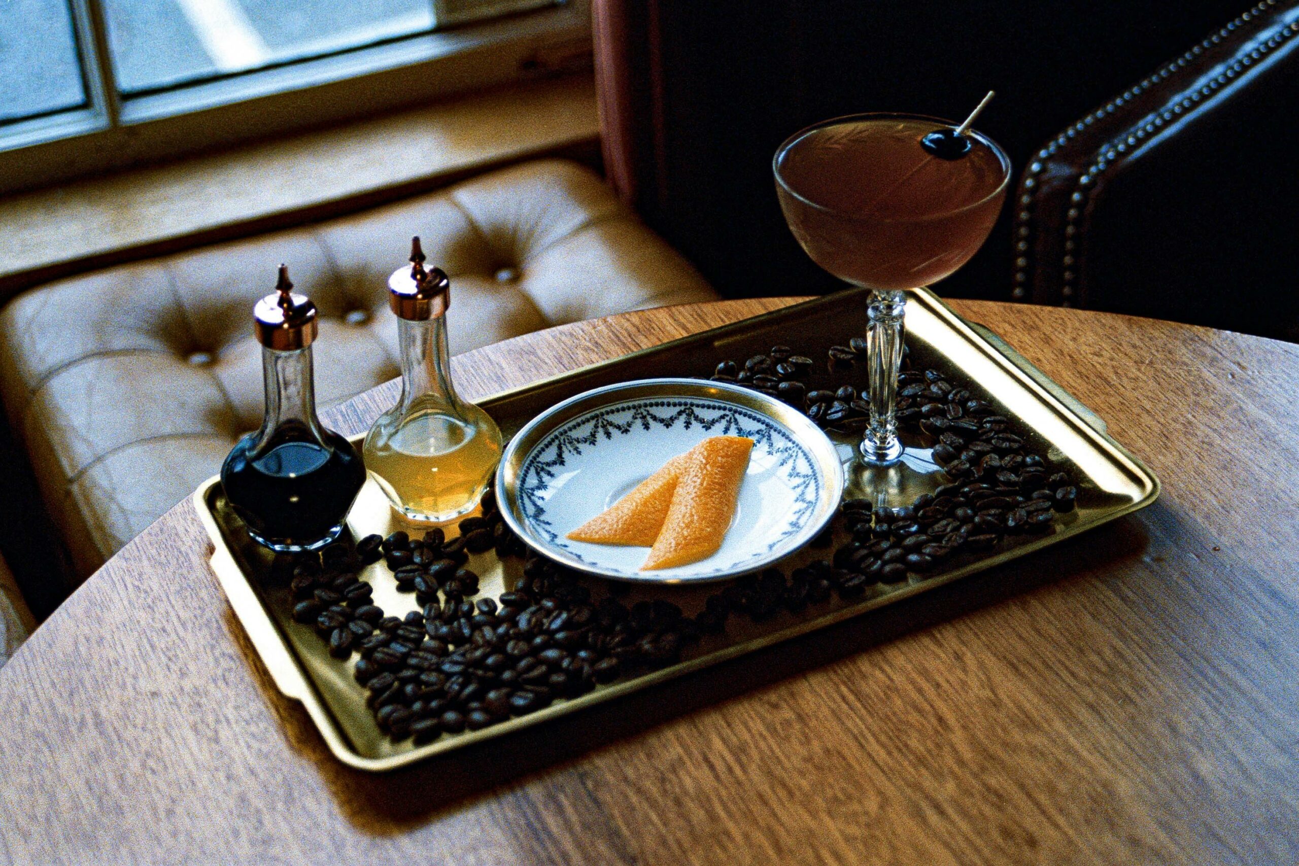 A sophisticated cocktail served on a tray with coffee beans and citrus garnish, exuding a classic vibe.